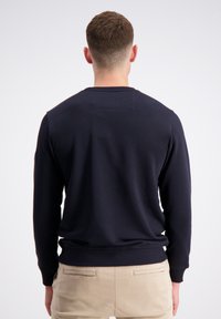 Granatowa bluza z długim rękawem i ściągaczami, z teksturowanym panelem z tyłu i prostym wzorem. Nosi się z jasnymi chinosami.