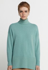 Ljust blå polotröja, tillverkad av mjukt stickat tyg, med ribbad textur vid ärmsluten och nederkant, med sänkt axelsöm.