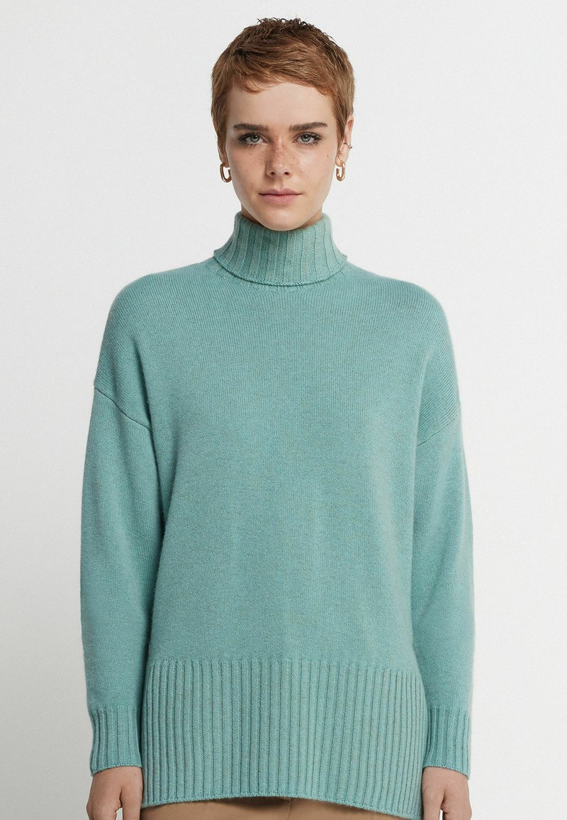 Ljust blå polotröja, tillverkad av mjukt stickat tyg, med ribbad textur vid ärmsluten och nederkant, med sänkt axelsöm.