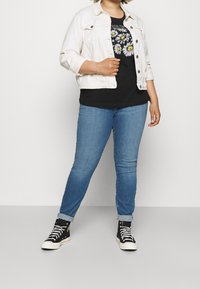 Biała jeansowa kurtka na czarnym t-shircie z kwiatowym wzorem, w połączeniu z jasnoniebieskimi jeansami skinny i czarnymi trampkami na wysokiej podeszwie.