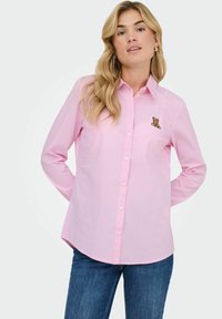 Camisa de botón a rayas rosas y blancas con un parche en el pecho de un oso; hecha de tejido ligero con un corte relajado y dobladillo curvado.
