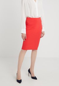 Jupe crayon rouge en tissu extensible, silhouette ajustée, texture lisse, assortie à une chemise blanche à boutons et des talons bleu marine.