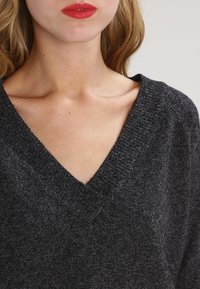 Dunkelgrauer V-Ausschnitt-Pullover aus strukturiertem Strickstoff, mit lockerem Schnitt und sichtbaren Nahtdetails am Ausschnitt.