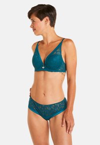 Brassière en dentelle turquoise avec des bonnets triangulaires, des bords festonnés et un matériel décoratif ; culottes hipster en dentelle assorties. Tissu doux, motif complexe.
