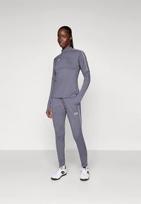 Siv športni dolg rokav in ujemajoče ozke hlače, izdelani iz zračnega materiala, z belimi poudarki in logotipom na prsih.