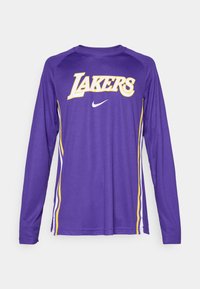 Chemise à manches longues violette avec "LAKERS" en jaune, logo Nike en blanc, et rayures jaunes et blanches sur les côtés. Texture de tissu lisse.