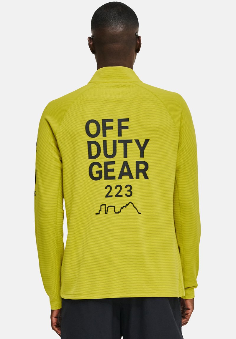 Langsleeve, felgele top met een gestructureerde afwerking. Kenmerkt zich door zwarte tekst "OFF DUTY GEAR 223" en een silhouetontwerp op de achterkant.