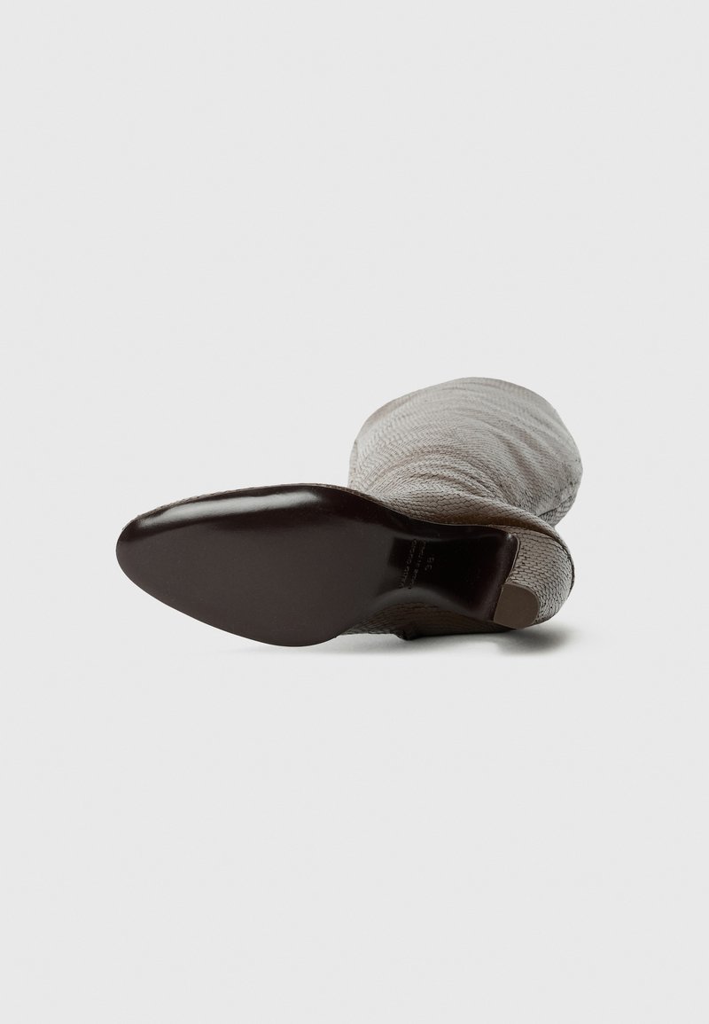 Graue gestrickte Knöchelstiefel mit einer glatten, dunkelbraunen Sohle. Obermaterial aus strukturiertem Stoff mit runder Zehe und schmalem Absatz.