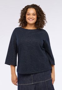 Pulover texturat de culoare albastru marin, cu mâneci până la cot și decolteu rotund. Țesătura are un luciu subtil și o croială lejeră.