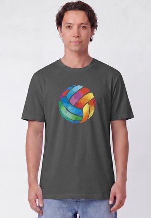 Jonge man draagt een donkergrijs T-shirt met een kleurrijk volleybalontwerp in aquarelstijl in het midden, staand tegen een effen achtergrond.