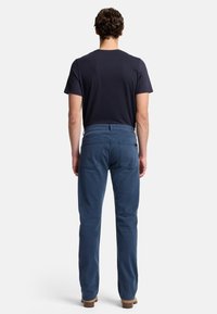 Pantaloni di cotone blu con design a gamba dritta, vita con passanti per cintura e tasche posteriori. Indossati con una camicia a maniche corte blu scuro.