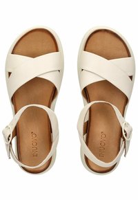 Bílé sandály s překříženými pásky a hnědou polstrovanou stélkou, s nastavitelným páskem a stříbrnou sponou. Hladká kožená textura.