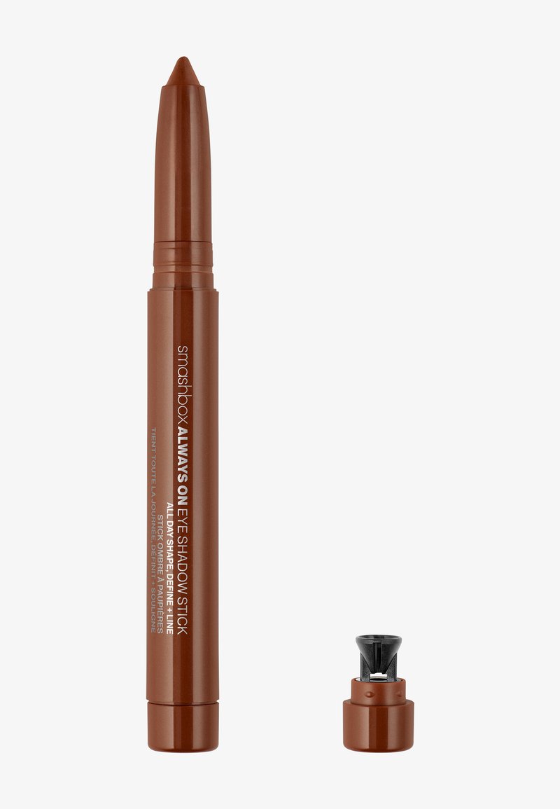 Brown eyeshadow stick with a tapered tip, featuring a twist-up mechanism. Cap includes a small black sharpener for precise application.