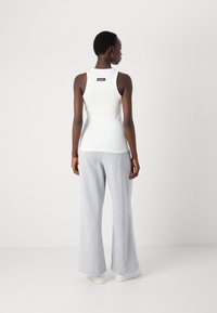 Hvit ribbet tanktopp med en svart etikett ved halsen, sammen med lysegrå vidbeinede joggebukser og hvite sneakers.