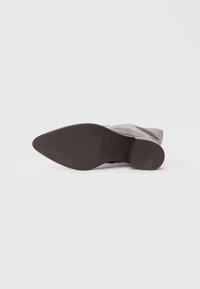 Botín de piel negra hasta el tobillo con textura suave, punta afilada, tacón bajo y suela de goma con líneas de agarre. Diseñado para la durabilidad y el estilo.