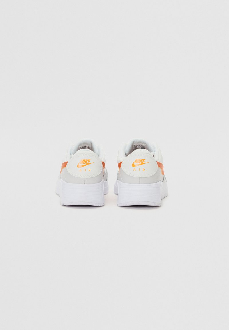 Zapatillas Nike con parte superior de cuero blanco, acentos naranjas en el talón y una suela de goma blanca texturizada. Marca visible en la parte posterior.
