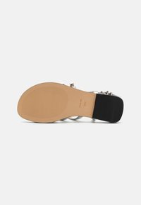 Svart og beige sandal såle med en jevn, strukturert overflate. Har et slankt stroppdesign med metalldetaljer og en flat hæl.