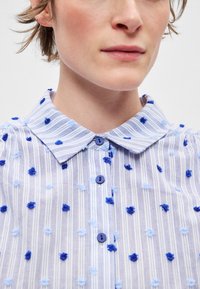 Ριγέ γαλάζιο πουκάμισο με μπλε και ανοιχτό γαλάζιες υφασμάτινες κουκκίδες, γιακά με μυτερή άκρη και κουμπιά σε μπλε χρώμα.