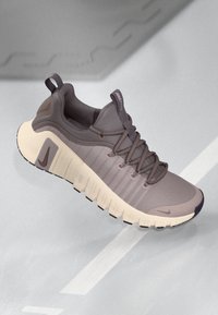 Nike Free παπούτσι σε γκρι χρώμα με υφασμάτινο επάνω μέρος με υφή, μαλακή κολάντζα και κρέμα ενδιάμεση σόλα. Διαθέτει καμπυλωτή εξωτερική σόλα και ασορτί κορδόνια.