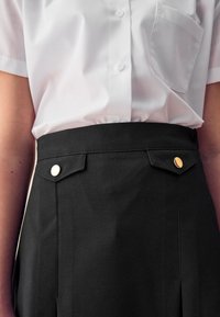 Sort højtaljet nederdel med guldtonede knapper og lommedetaljer, parret med en hvid kortærmet knappet skjorte. Glat tekstur.