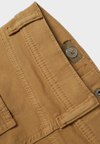 Tejido de algodón color marrón claro con detalles de costura, cierre de botón y presilla para cinturón en la parte superior. Textura suave con un color sólido.