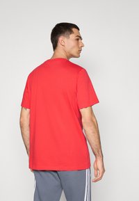 Rød bomulds T-shirt med korte ærmer og rund halsudskæring, der viser en afslappet pasform. Bagfra ses en glat tekstur uden synlige logoer.