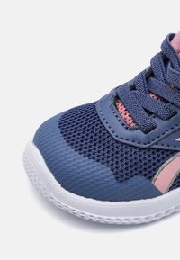 Zapatilla de malla azul con detalles en rosa, suela media texturizada y cordones planos. Cuenta con un cuello acolchado y tejido transpirable para mayor comodidad.