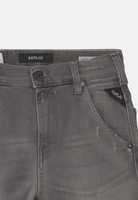 Šedé džíny z denimu s knoflíkovým zapínáním, se zašlými akcenty a logem na pásku. Obsahuje přední a zadní kapsy.