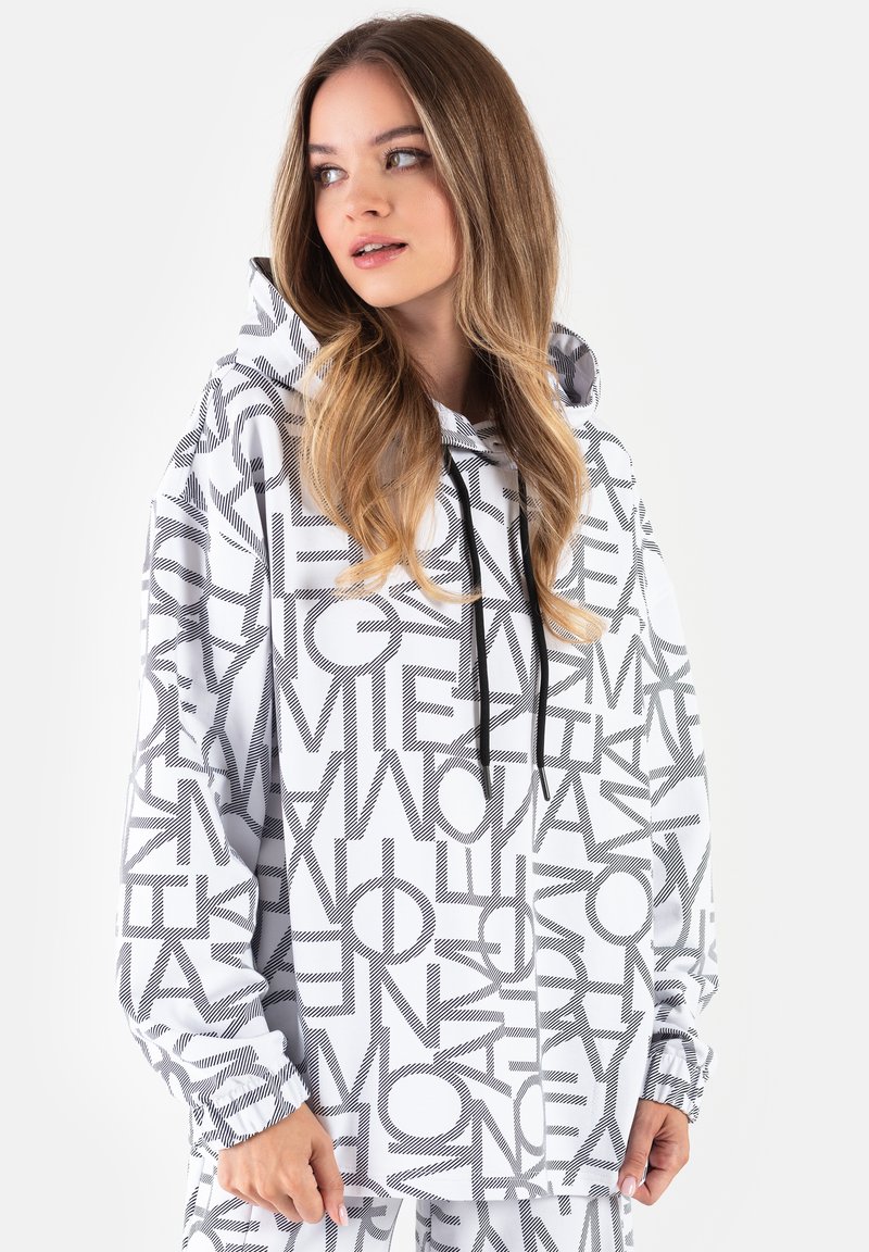 Biała bluza z kapturem z dużymi czarnymi napisami graficznymi, posiadająca kaptur ze sznurkiem, długie rękawy i elastyczne mankiety. Gładka faktura tkaniny.