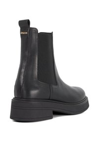 Zwarte leren Chelsea-boot met dikke zool, elastische zijpaneel, aantrekloop en klein gouden "Dune" logo aan de achterkant.