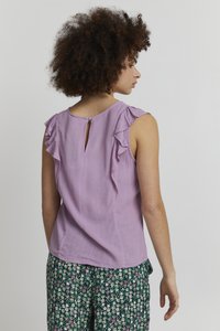 Top senza maniche in lavanda con spalline arricciate, dotato di scollo tondo e un piccolo bottone a chiave sul retro. Tessuto testurizzato.