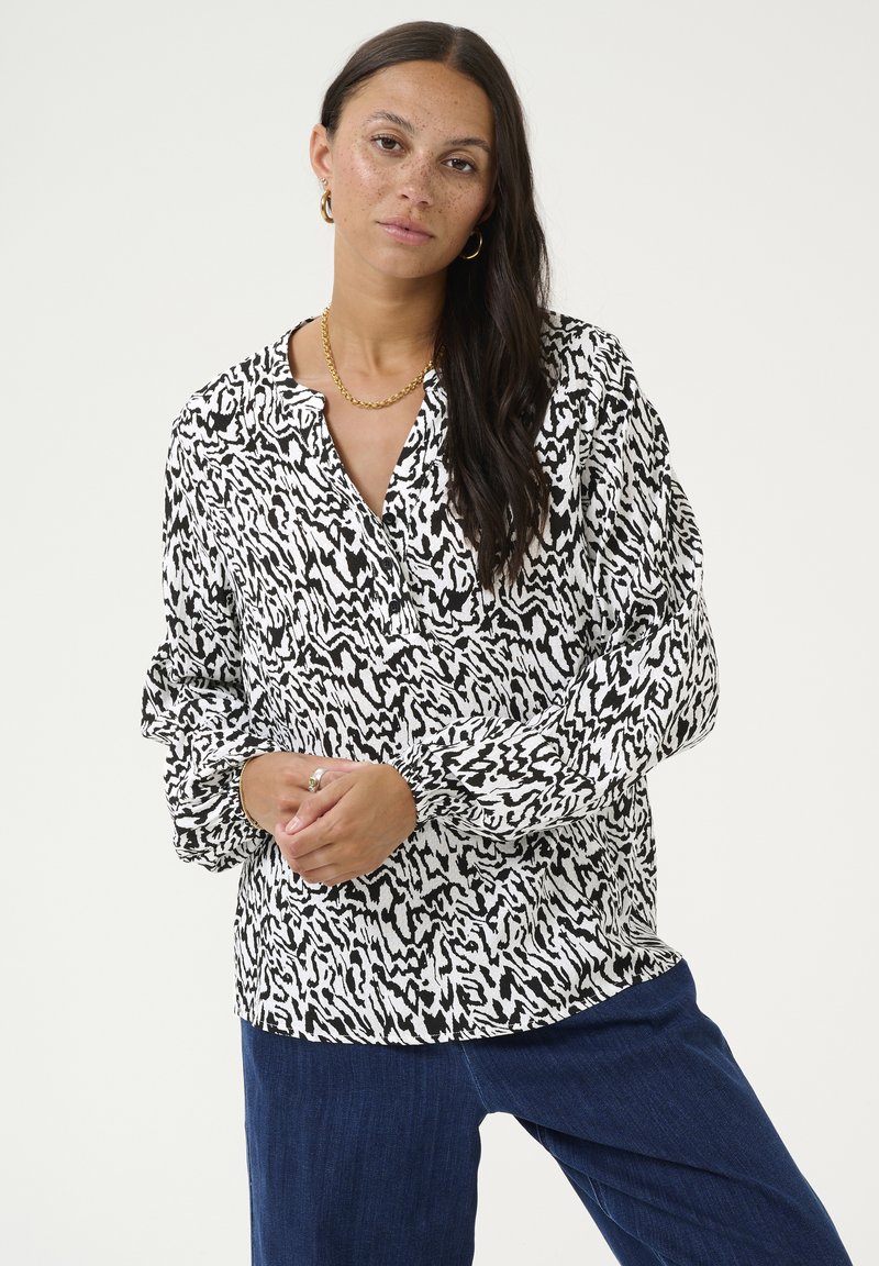 Blouse à motif noir et blanc avec une coupe décontractée, des manches longues et un col sans col, fabriquée à partir d'un tissu léger.
