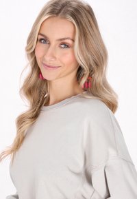 Felpa grigia chiara con scollo a giro e spalle scese. Presenta una texture morbida e maniche aperte e svasate. Accessoriata con orecchini rosa vivaci.