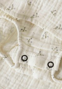 Morbidi indumenti bianchi per bambini con piccoli motivi floreali blu e bottoni automatici neri su tessuto strutturato.