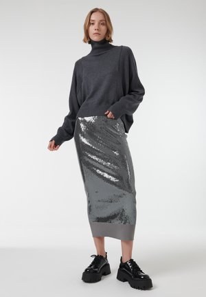 Grijze coltrui met verlaagde schouders, in combinatie met een aansluitende midirok in zilveren pailletten. Dikke zwarte veterschoenen maken de look compleet.