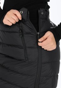 Svart isolerad kjol med quiltat mönster, framtill dragkedja med knappstängning och två sidofickor med dragkedja för förvaring.