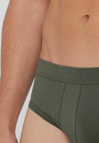 Oliwkowe bawełniane bokserki z szerokim elastycznym pasem, płaskimi szwami i dopasowanym krojem, sięgającym do górnej części uda.