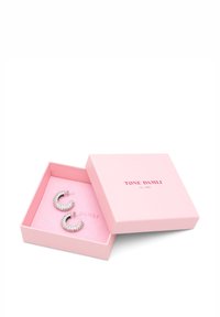 Sølv creoler med et rundt design, prydet med klare krystaller, præsenteret i en blød lyserød æske med brandlogo.