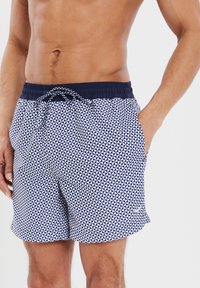 Pantaloni da bagno blu e bianchi con un motivo geometrico a triangolo. Presentano una vita elasticizzata con cordoncino e tasche laterali.