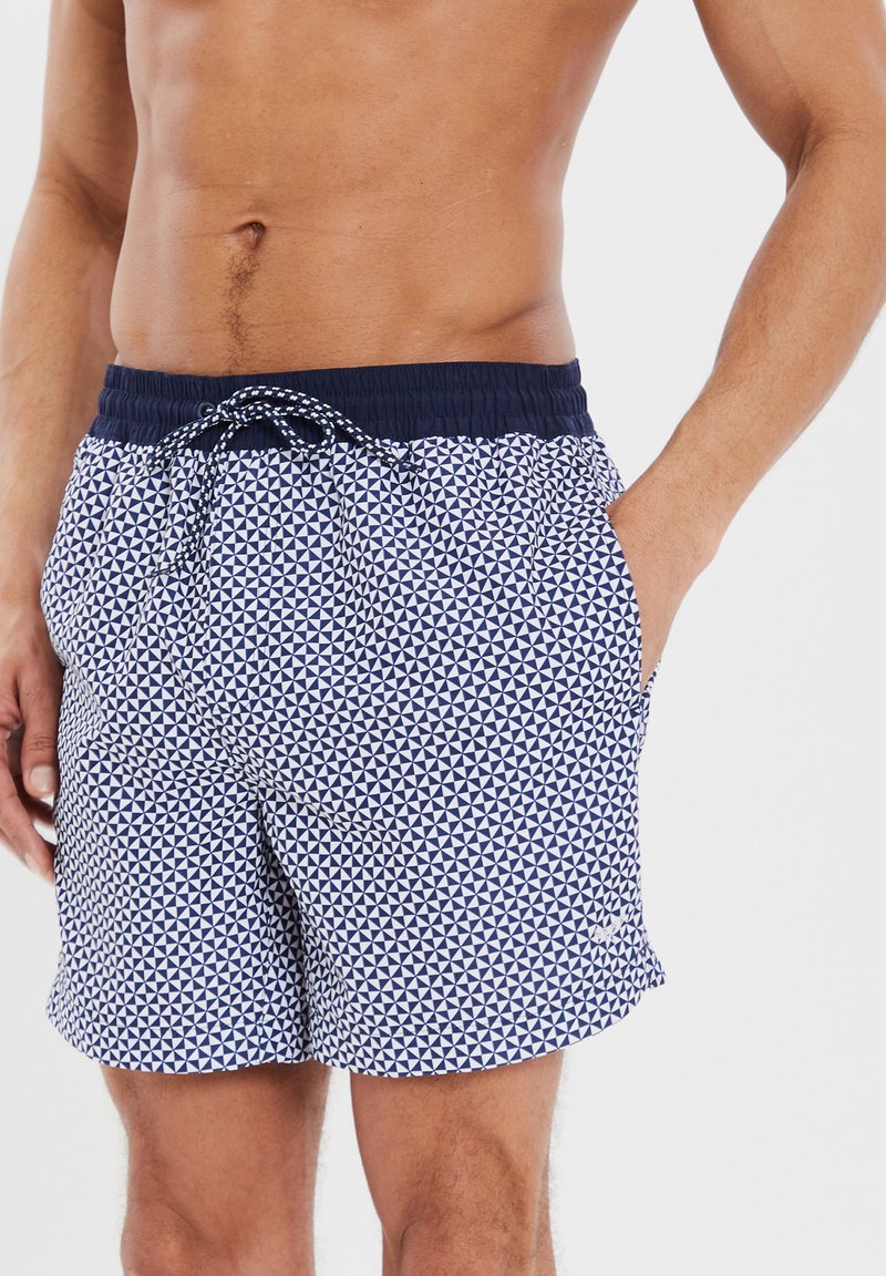 Pantaloni da bagno blu e bianchi con un motivo geometrico a triangolo. Presentano una vita elasticizzata con cordoncino e tasche laterali.
