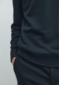 Maglione blu navy scuro con una texture liscia e polsini a coste, abbinato a pantaloni a righe sottili, enfatizzando un look monocromatico coerente.