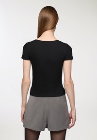 Czarny prążkowany top z krótkim rękawem, dopasowany krój, okrągły dekolt, zestawiony z szarymi szortami, gładka faktura, styl casual.