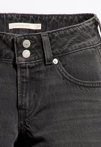 Black denim superlow loose jeans with a textured finish, featuring two metal buttons at the waist and a label indicating size 27.