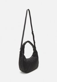 Sac à épaule noir matelassé avec une petite anse et une longue sangle réglable, doté d'une fermeture éclair et d'un motif de coutures en forme de diamant.