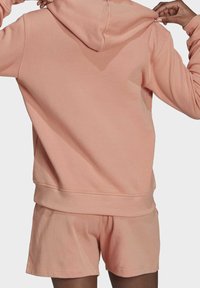 Ljusrosa huvtröja med mjuk textur, med en kenguruficka och ribbad nederkant, i kombination med matchande shorts.