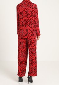 Czerwony satynowy garnitur w wzór panterki, z długim rękawem i szerokimi spodniami. Czarny akcent na butach.