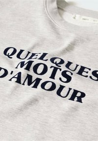 Tissu gris clair avec texte noir indiquant "QUELQUES MOTS D'AMOUR" en lettres majuscules et en gras.