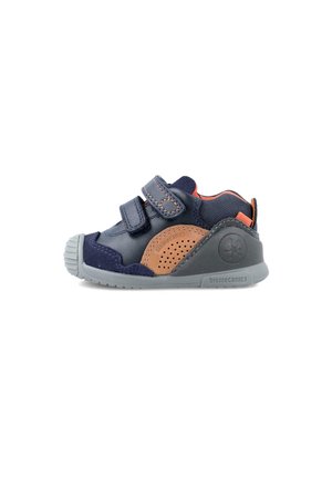 Zapato infantil azul y marrón con correas de Velcro, paneles perforados y una suela de goma gris. Presenta detalles de cuero texturizado y acentos de malla.