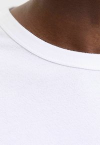 Col haut de t-shirt en coton blanc avec une texture lisse, présentant un design côtelé et des bords sans couture, gros plan sur un fond de teinte de peau.