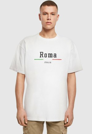 Hvit t-skjorte med rund hals som har "Roma" i fet svart tekst og "ITALIA" nedenfor, aksentuert med grønne og røde horisontale linjer.
